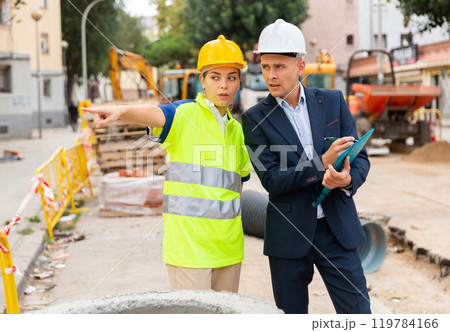 Young woman worker on a construction site shows something to a man engineer Young woman worker on a construction site shows something to a man engineer 119784166