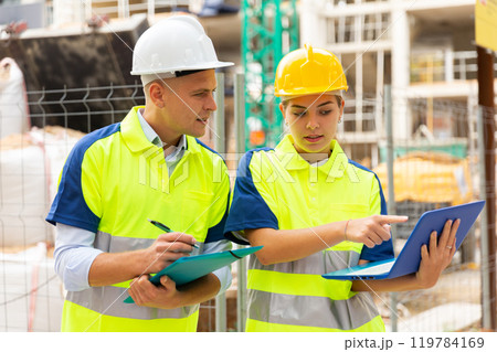 Two engineers are discussing an important project, holding a laptop and an estimate Two engineers are discussing an important project, holding a laptop and an estimate 119784169