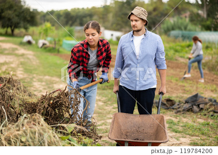 Woman and man takes out bunch of branches, puts garbage in wheelbarrow Woman and man takes out bunch of branches, puts garbage in wheelbarrow 119784200