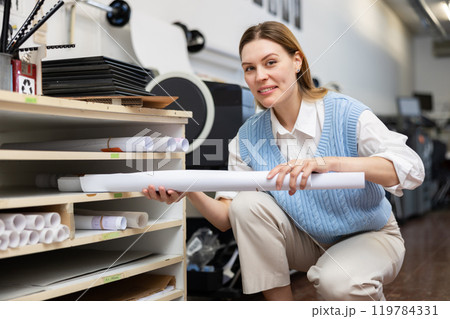 Woman employee at copy center putting roll paper on shelves 119784331