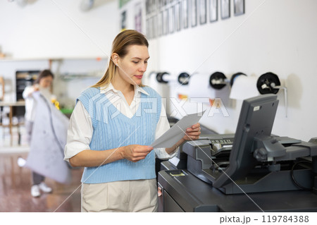 Woman checking paper after printing 119784388