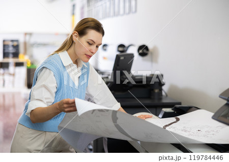 Female employee of the printing house checks the quality of the print Female employee of the printing house checks the quality of the print 119784446