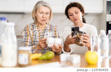 Adult daughter and elderly mother scan barcode on food package together using smartphone Adult daughter and elderly mother scan barcode on food package together using smartphone 119784450