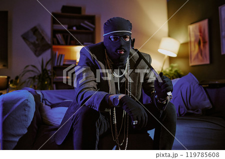 Portrait of unrecognizable thief in jacket and golden pearl necklaces holding metal crowbar and looking at camera Portrait of unrecognizable thief in jacket and golden pearl necklaces holding metal crowbar and looking at camera 119785608
