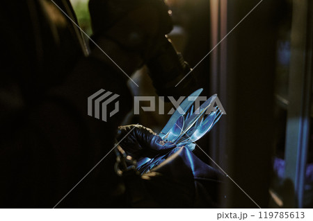 Medium close up of unrecognizable thies hands in black leather gloves holding silverware under flashlight 119785613