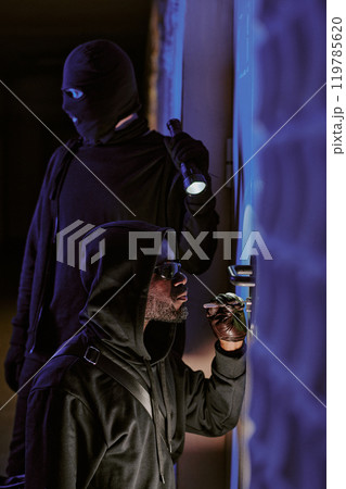 Vertical shot of two crime partners picking lock together at late night trying to enter house 119785620