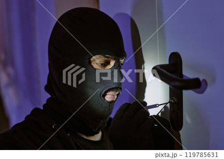 Medium close up of unrecognizable thief picking lock and listening to doors click at night 119785631