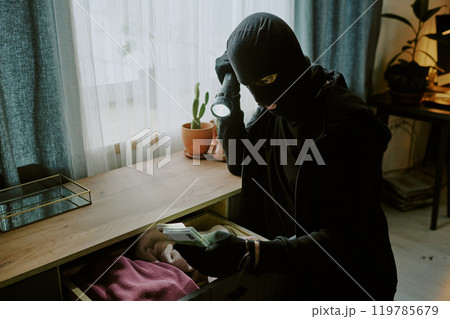 Male unrecognizable thief with flashlight holding packs of money in living room during trespassing Male unrecognizable thief with flashlight holding packs of money in living room during trespassing 119785679