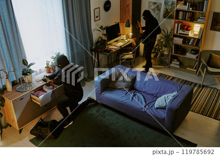 High angle shot of crime partners stealing fashionable clothes and digital device in spacious living room High angle shot of crime partners stealing fashionable clothes and digital device in spacious living room 119785692