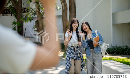 Two friendly Asian students are saying goodbye to their friend while walking in their college. Two friendly Asian students are saying goodbye to their friend while walking in their college. 119785758