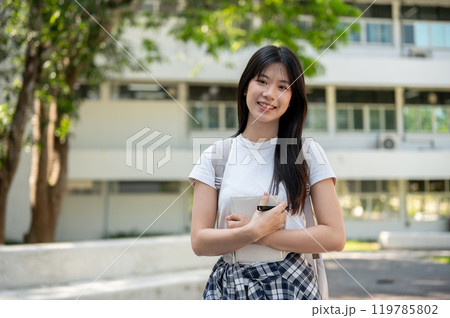 A cute Asian female college student standing on her college campus, smiling at the camera. A cute Asian female college student standing on her college campus, smiling at the camera. 119785802