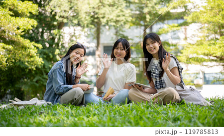 Charming Asian female college students are sitting together in a park, smiling at the camera. 119785813