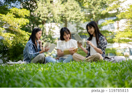 A group of female college students is sitting together on the grass, enjoying reading together. A group of female college students is sitting together on the grass, enjoying reading together. 119785815