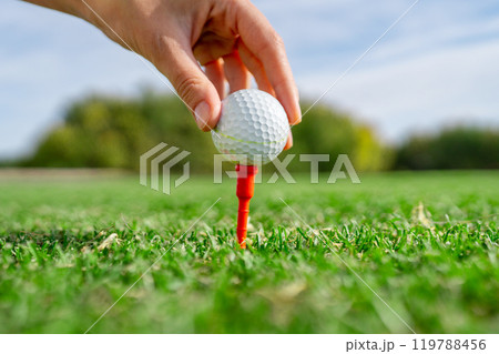 Carefully Hand Placing a Golf Ball on a Tee Under a Beautiful Blue Sky on a Sunny Day 119788456
