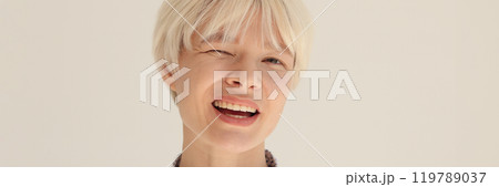 Cheerful blonde woman in shirt winks slyly in light office 119789037