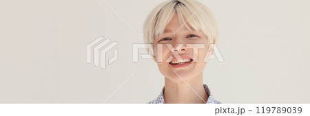 Positive blonde female smiles while standing in bright room 119789039