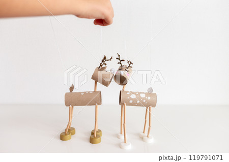 Hand holding wooden stick controlling DIY reindeer puppets crafted from recycle toilet paper roll cardboard tubes and bottle caps. Minimalistic shot for Christmas holiday craft concept. 119791071