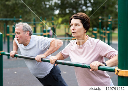 Elderly couple doing push-ups on crossbar together on sports ground of city park 119791482