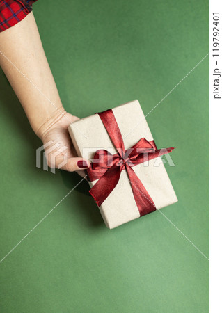 a female hand with a burgundy manicure holds a gift box with a burgundy bow a female hand with a burgundy manicure holds a gift box with a burgundy bow 119792401