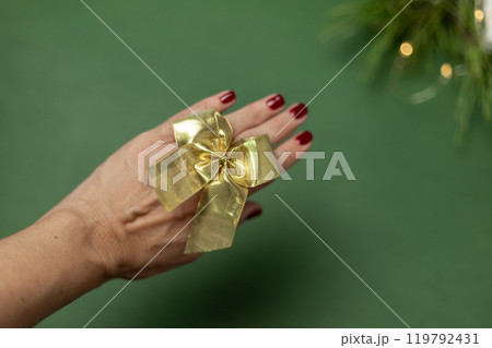 golden bow on a hand with a red manicure on a green background 119792431