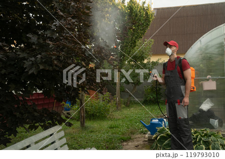 Gardener wearing mask spraying trees in garden Gardener wearing mask spraying trees in garden 119793010