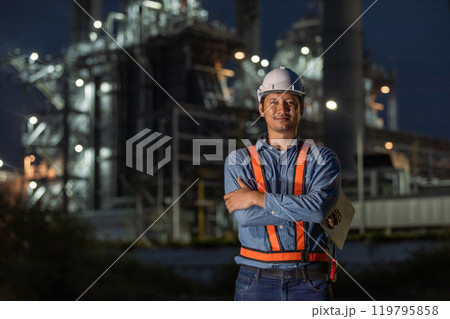 portrait of asian man engineer working at nighttime standing at front of Oil-fired power plant. Worker wear uniform helmet working tower power plant construction. portrait of asian man engineer working at nighttime standing at front of Oil-fired power plant. Worker wear uniform helmet working tower power plant construction. 119795858