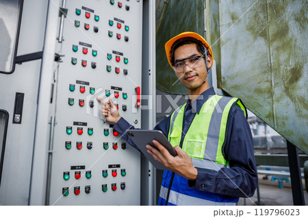 Electrical engineer man using tablet checks switchboard main Distribution Boards control panel electric factory building. Male Industrial technician worker working power distribution room. 119796023