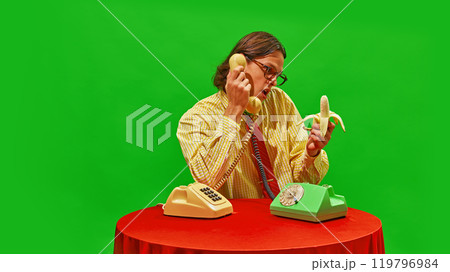 Man want to eat banana while talking on two vintage phones, adding quirky and humorous twist to office scene. Man want to eat banana while talking on two vintage phones, adding quirky and humorous twist to office scene. 119796984