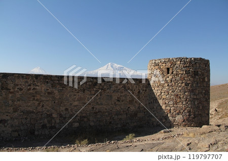 Ancient castle ruin with snow-capped mountain in the distance on horizon under clear blue sky Ancient castle ruin with snow-capped mountain in the distance on horizon under clear blue sky 119797707