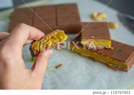 Piece of trend Dubai chocolate with pistachio paste and kataifi dough in woman hand. Confectionery handmade sweets at home in the kitchen.  119797801