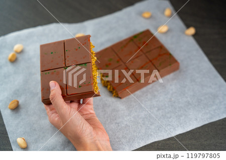 Trend Dubai chocolate with pistachio paste and kataifi dough in woman hands. Confectionery handmade sweets at home in the kitchen. Trend Dubai chocolate with pistachio paste and kataifi dough in woman hands. Confectionery handmade sweets at home in the kitchen. 119797805