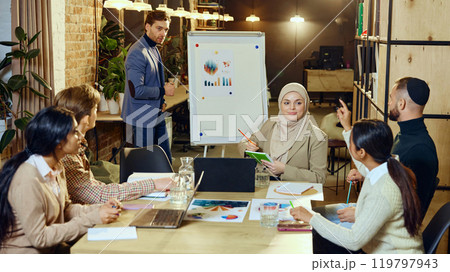 Diverse group of young professionals gathered around table, discussing and working together on project. 119797943