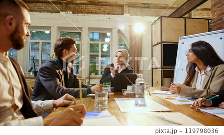 Diverse group of business people discussing presentation on company growth, led by female presenter in hijab. Diverse group of business people discussing presentation on company growth, led by female presenter in hijab. 119798036