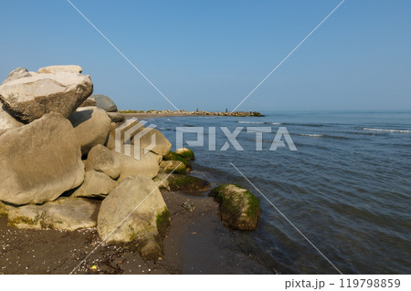 Large rocks on the shore of the Caspian Sea. In the background, fishermen stand on the shore and fish with a rod. 119798859
