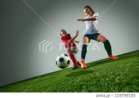 Competitive and motivated young women, soccer players in dynamic motion, competing on field over control of ball. Under rainy weather Competitive and motivated young women, soccer players in dynamic motion, competing on field over control of ball. Under rainy weather 119799185