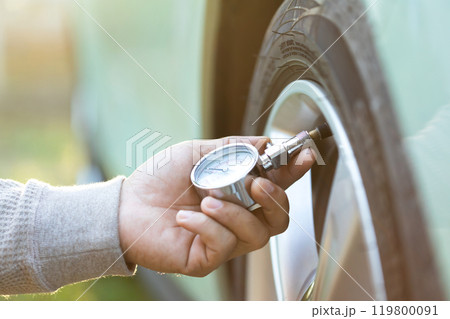Car owner uses a pressure gauge to check tire inflation, emphasizing vehicle readiness and the importance of proper tire maintenance before embarking on a journey Car owner uses a pressure gauge to check tire inflation, emphasizing vehicle readiness and the importance of proper tire maintenance before embarking on a journey 119800091