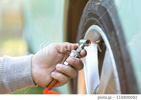 Car owner inflates a tire, highlighting the importance of tire maintenance and pressure checks to ensure safe, smooth travel and readiness before a journey 119800092