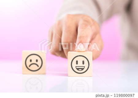 A man choosing between a happy and sad face on wooden blocks, ultimately selecting the happy one. The concept of starting each day with positivity, emphasizing the importance of a bright outlook 119800097