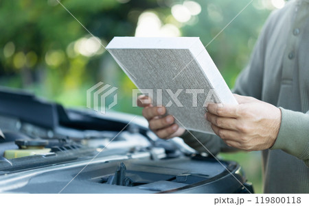 Car owner holds an air filter for examination. Importance of regular inspection, cleaning, and replacement of car air filters, Emphasizes maintenance for better air quality and vehicle efficiency 119800118