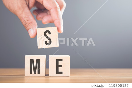 A hand arranging wooden blocks with the letters 'SME' on a table, set against a gray background. Concept of small and medium-sized enterprises, highlighting their importance in the business landscape A hand arranging wooden blocks with the letters 'SME' on a table, set against a gray background. Concept of small and medium-sized enterprises, highlighting their importance in the business landscape 119800125