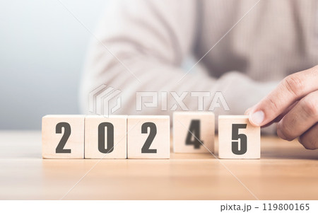 Hand replaces "2024" with "2025" using number blocks, symbolizing the transition into the new year, representing change, progress, and the ongoing passage of time Hand replaces "2024" with "2025" using number blocks, symbolizing the transition into the new year, representing change, progress, and the ongoing passage of time 119800165