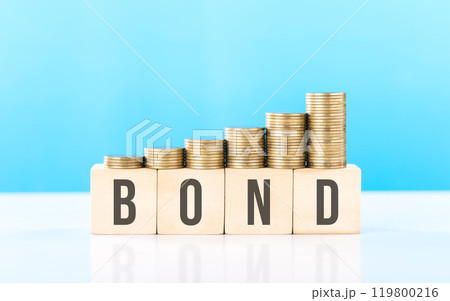 Stack of various types coins alongside a wooden block labeled BOND. Steady and structured growth linked to bond investments, highlighting stability and the importance of long-term financial planning Stack of various types coins alongside a wooden block labeled BOND. Steady and structured growth linked to bond investments, highlighting stability and the importance of long-term financial planning 119800216