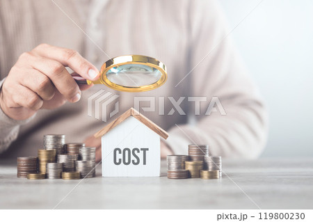 Stack of coins, a house model, and a hand holding a magnifying glass. The concept of evaluating home repair costs, highlighting the importance of careful financial assessment and budgeting 119800230
