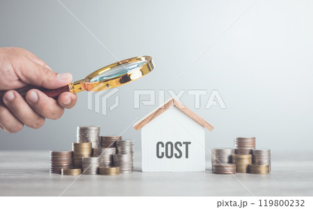 Stack of coins, a house model, and a hand holding a magnifying glass. The concept of evaluating home repair costs, highlighting the importance of careful financial assessment and budgeting 119800232