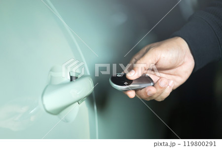 A man's hand holding a car remote to unlock the vehicle. The image represents the concept of using a car remote, highlighting the role of remote battery power in accessing and securing the car A man's hand holding a car remote to unlock the vehicle. The image represents the concept of using a car remote, highlighting the role of remote battery power in accessing and securing the car 119800291