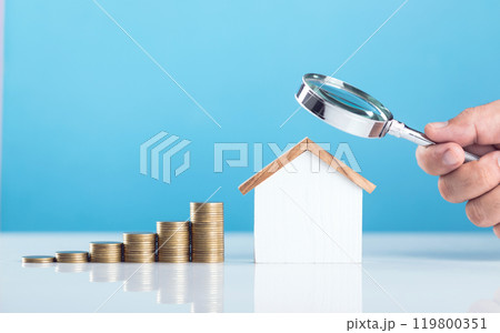 A wooden house model next to a stack of coins, with a hand holding a magnifying glass over them. The image represents the concept of analyzing and calculating home maintenance and repair costs A wooden house model next to a stack of coins, with a hand holding a magnifying glass over them. The image represents the concept of analyzing and calculating home maintenance and repair costs 119800351