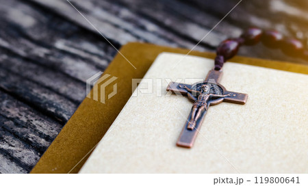 Shiny copper cross leaning against an old open book symbolizing the spread of Jesus Christs love among Christians reflecting faith devotion and the importance of Christian teachings. 119800641