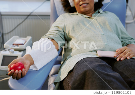 Person lying comfortably while donating blood in modern medical facility. Patient holding stress ball with bandage on arm, suggesting calm and cooperative feeling Person lying comfortably while donating blood in modern medical facility. Patient holding stress ball with bandage on arm, suggesting calm and cooperative feeling 119801105