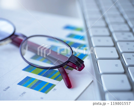 テーブルに置かれたグラフとキーボードとメガネ 119801557