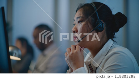 Mental health line: Close up portrait of Asian hotline specialist in headset listening person Mental health line: Close up portrait of Asian hotline specialist in headset listening person 119803298